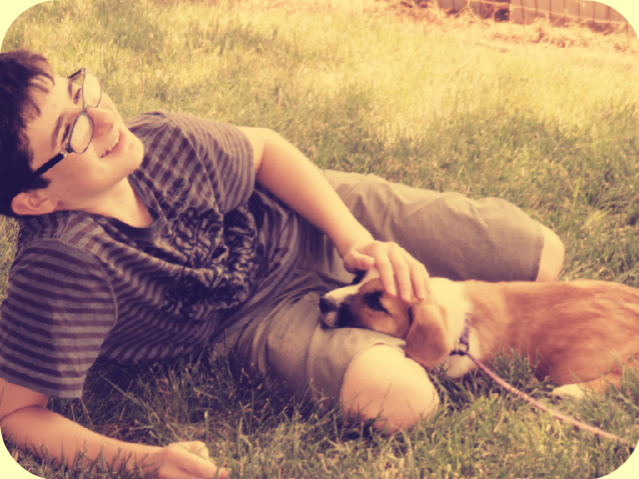 little boy lying in grass with puppy's head resting on his leg 