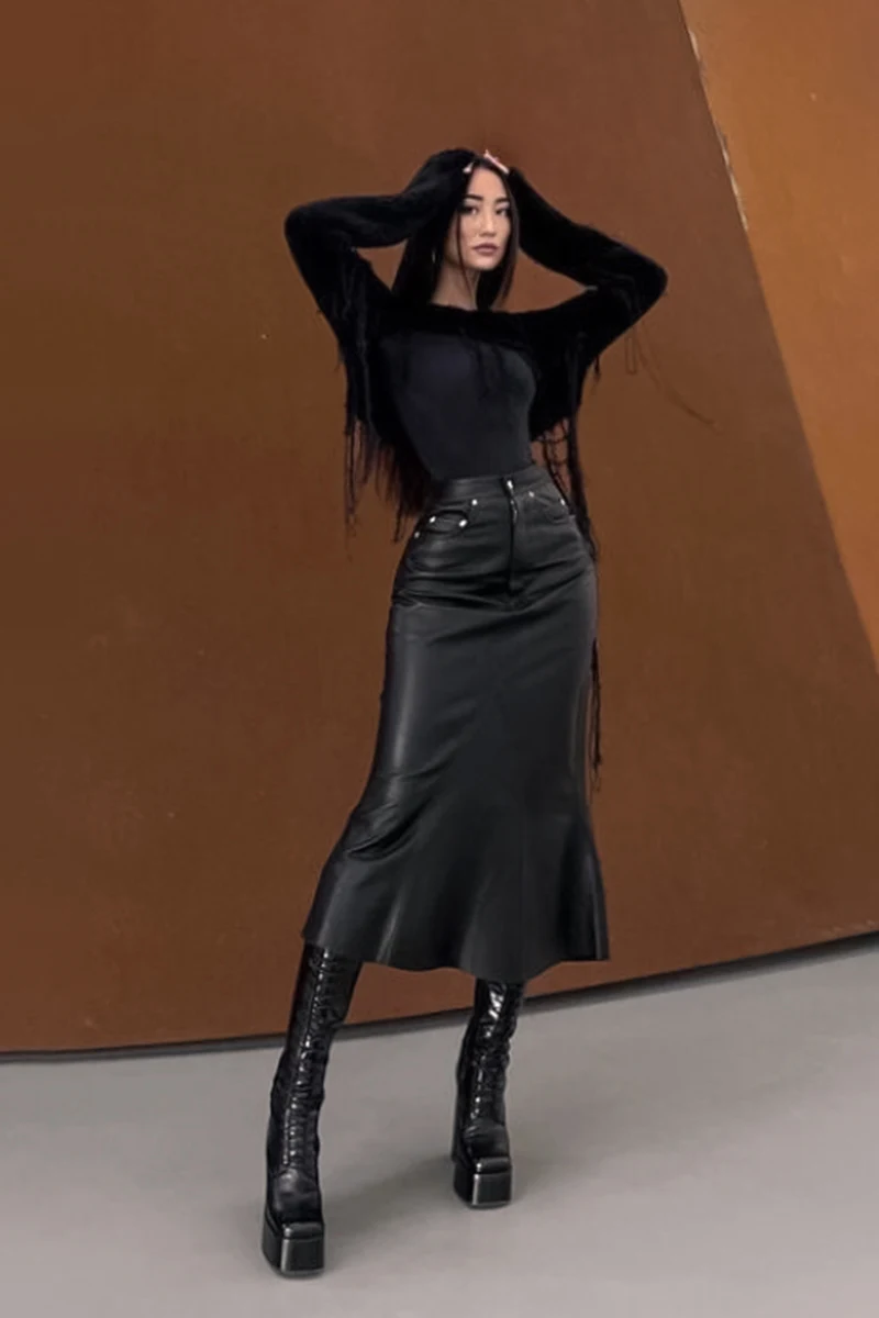 stylish young woman in total black outfit is posing for the camera on a street