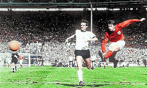 A grainy colour photograph of striker Geoff Hurst blasting a shot past a German defender - the final goal of England's 4-2 victory over Germany in the 1966 World Cup Final