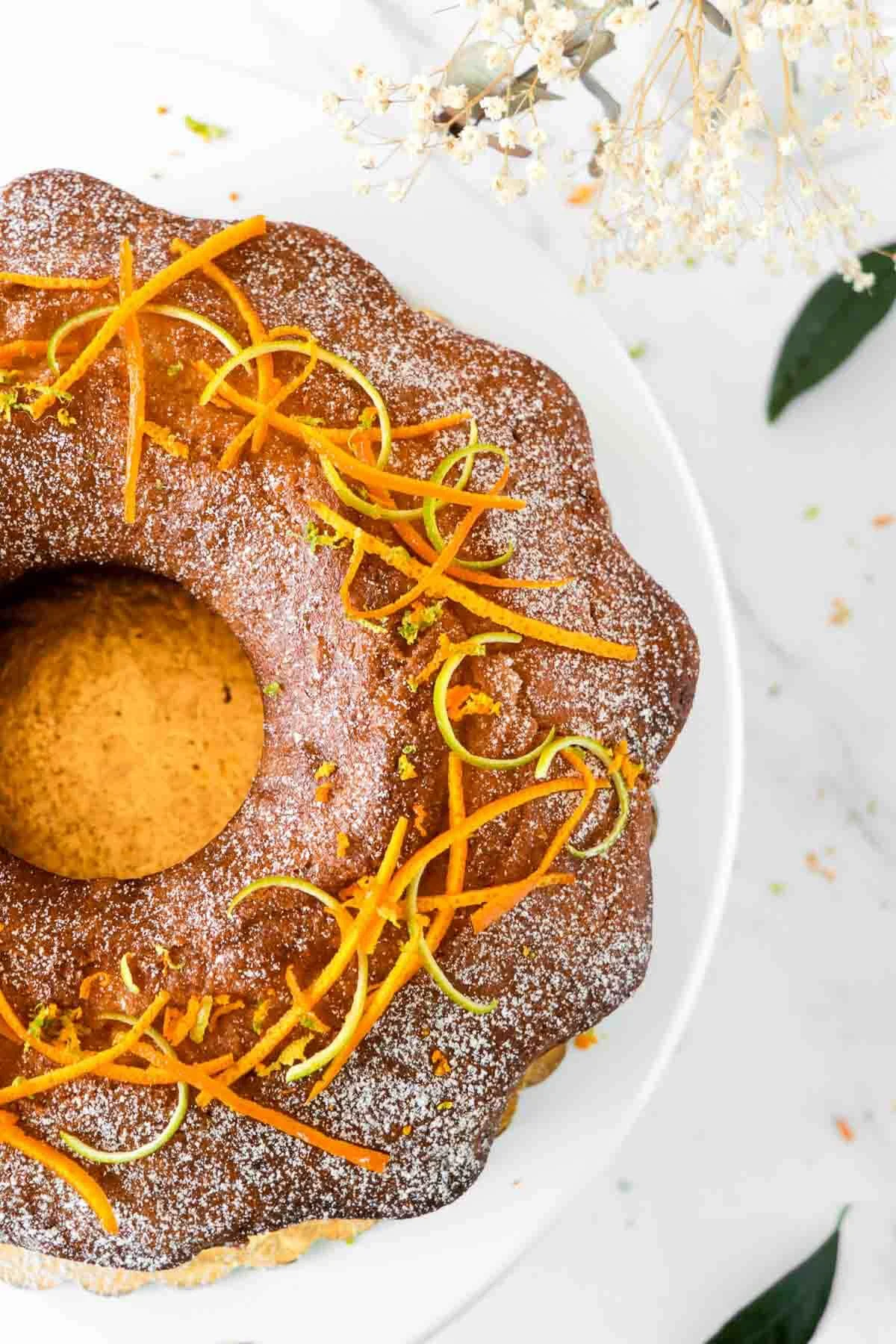 Overhead shot of an orange rum cake on a white cake stand decorated with powder sugar and citrus rinds.
