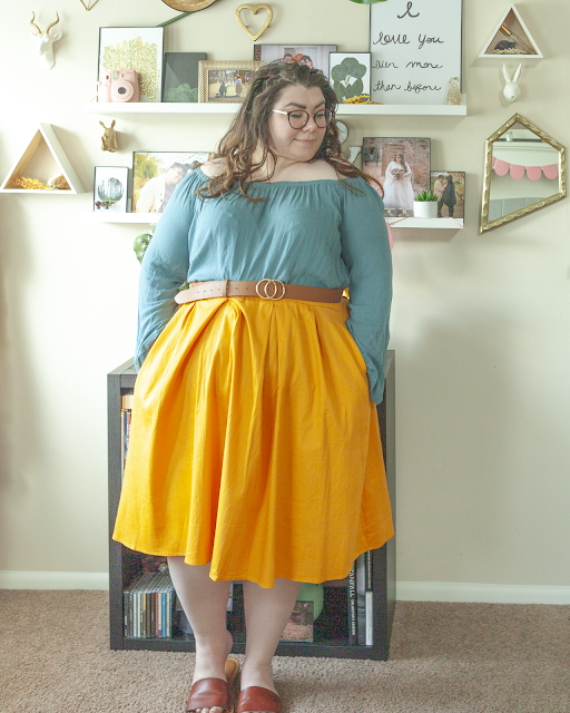 An outfit consisting of a Turkish blue off the shoulder blow with bell sleeves tucked into a yellow midi skirt and brown slide sandals.