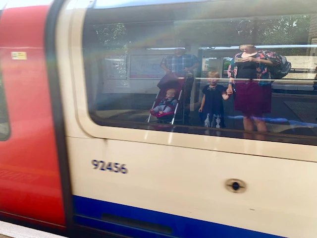 A tube train pulling into a station with the reflection of a family in the window