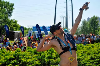 With finisher medal, nutrition and race belt around my neck only wearing my heart rate strap; I point one arm to the sky while flexing the other 