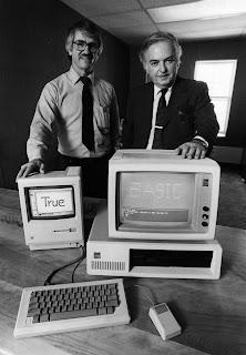 A photograph of two men by a pair of computers, the screens reading "True" and "Basic."