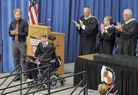 People applauding for Justin who is driving in his wheelchair after graduation speech