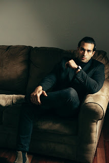 A man sitting on a sofa in a room, appearing calm and at ease.