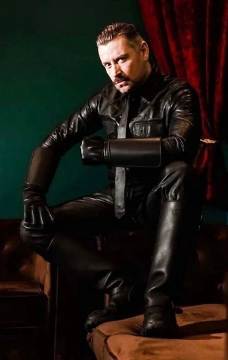 Handsome mustache man sitting down wearing full black leather outfit with tie and gloves