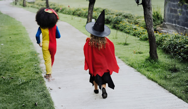 Two children walking away along a path, with one wearing a red cape and a witches hat and one as a clown in a onesie