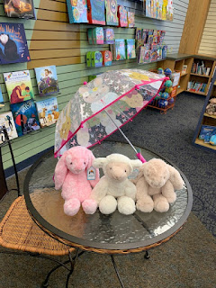 plush bunnies and a plush lamb sit under an clear umbrella with pink trim and pastel cartoon mice