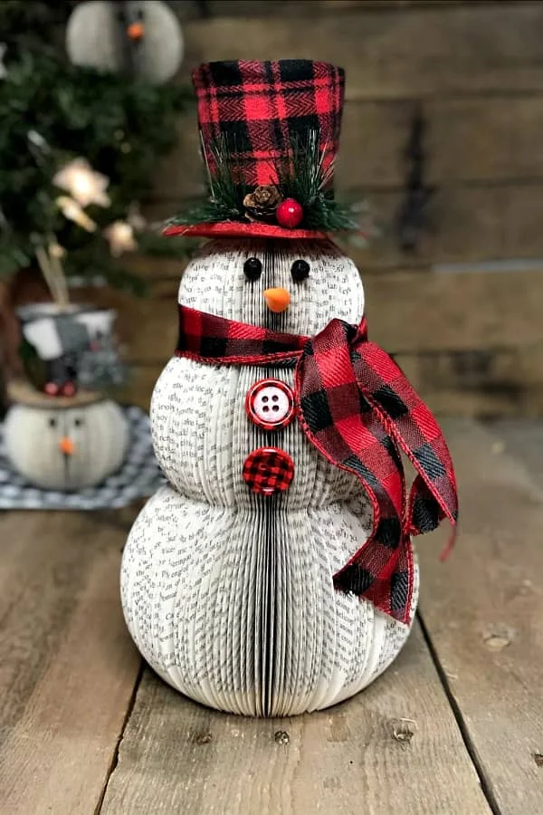 altered book snowman wearing plaid scarf and top hat placed in front of small snowman tree ornament