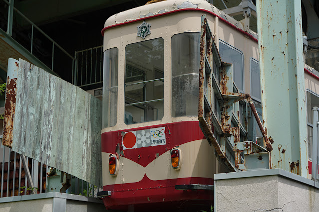 도색이 벗겨지고 녹이 슨 철제 구조물 사이로 낡은 곤돌라가 보인다. 곤돌라 앞면에는 1972년 삿포로 올림픽 로고가 붙어있다.