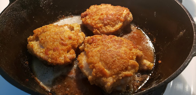 Black cast iron skillet with three pieces of chicken cooking