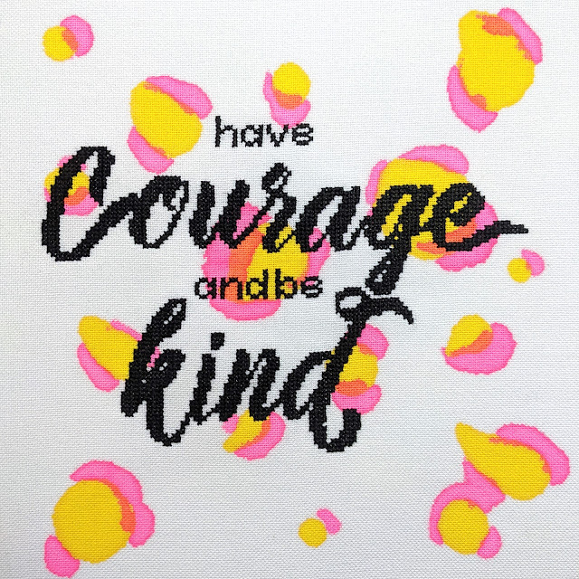 cross stitch lettering in modern calligraphy font with the words 'have courage and be kind' stitched on white fabric with pink and yellow leopard print