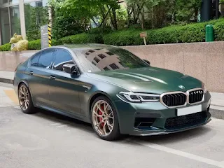 "BMW F90 M5 CS in Frozen Deep Green Metallic parked on a scenic road"