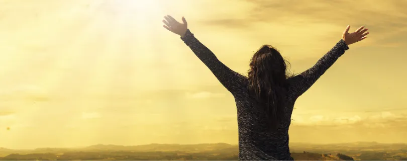 Mulher com as mãos erguidas em direção aos céus. Representação de esperança.