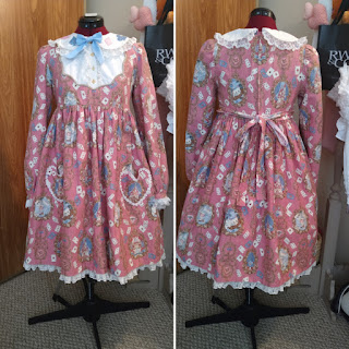 A front and back view of the wonder memories op. The front has heart shaped pockets and bell sleeves. The collar of the op (which is long sleeved) has the card suit on it.