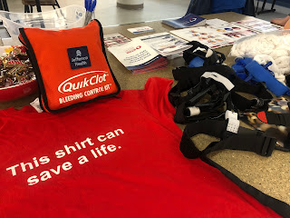 Our Stop the Bleed training table, containing a first aid kit, a tourniquet, and a t-shirt that says "This shirt can save a life."