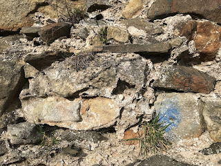 A photo of a crumbling stone wall.  In the centre, in the crumbling cement, is a small, ceramic skull (Skulferatu 96).  Photograph by Kevin Nosferatu for the Skulferatu Project.