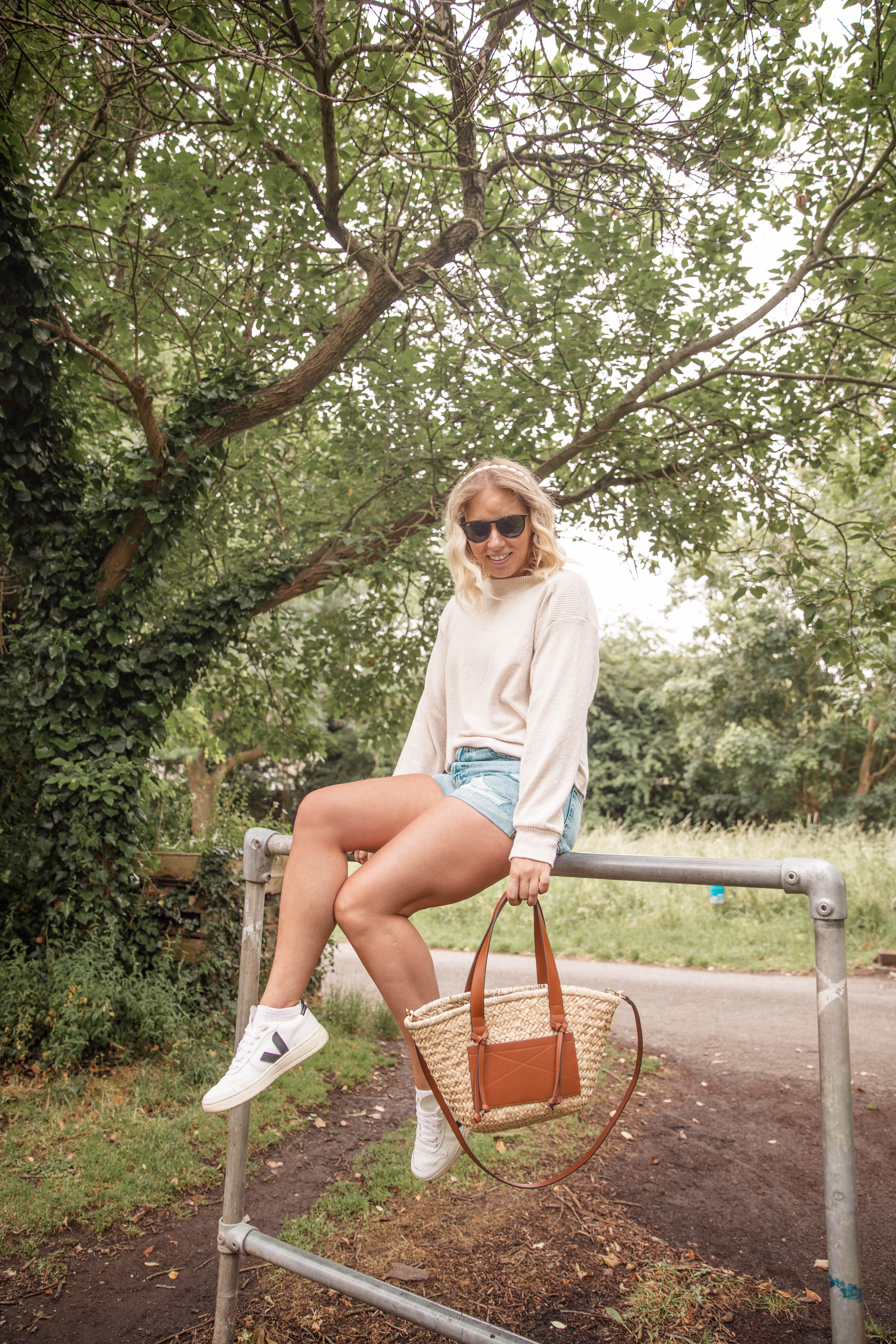 Rachel Emily wearing a beige jumper, denim shorts and the mango tan basket bag whilst sitting