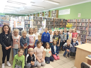 Zdjęcie grupowe. Przedszkolaki stoją przed ladą biblioteczną. Tło: regały z książkami.