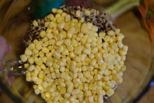 Frozen corn added to the bowl with the grains.