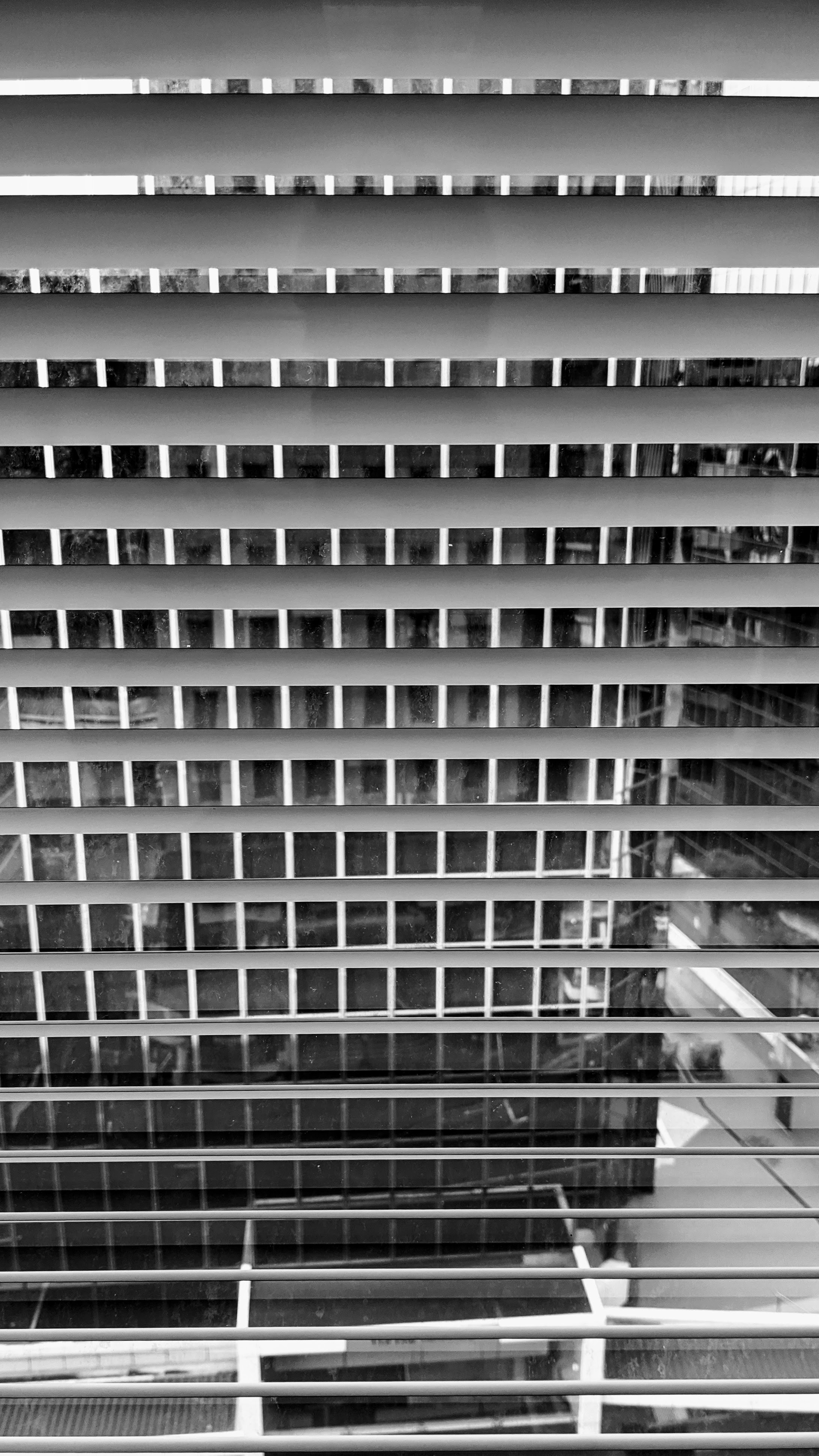 Black and white photo of horizontal blinds against the windows of a vertical building