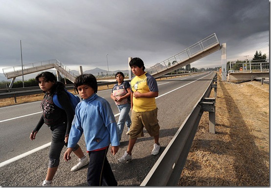 People walk along a highway with a collapsed bridge in the background in the outskirts of Santiago after a huge 8.8-magnitude earthquake rocked Chile early killing at least 78 people, on February 27, 2010. The massive quake plunged much of the Chilean capital, Santiago, into darkness as it snapped power lines and severed communications, and AFP journalists spoke of walls and masonry collapsing. People in pyjamas fled onto the streets. AFP PHOTO/MARTIN BERNETTI (Photo credit should read MARTIN BERNETTI/AFP/Getty Images)