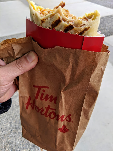 Hubby holding a Tim Hortons bag. Inside the bag is a Farmers Breakfast Wrap.