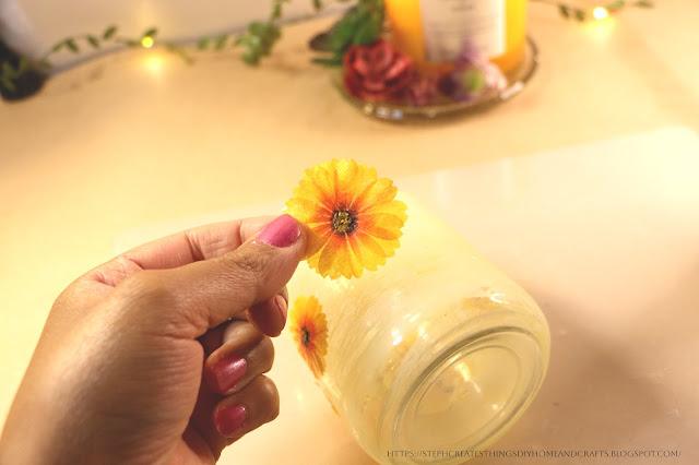 Hand holding up a yellow paper flower above painted glass jar