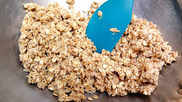 the granola mix for M & M Granola Bars sitting in a large stainless steel bowl with a teal colored spatula