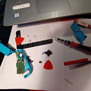 A torn apart Nintendo Switch Joycon; Neon Blue, sits on a piece of paper beneath a laptop; the paper says RUNTCPIP.com