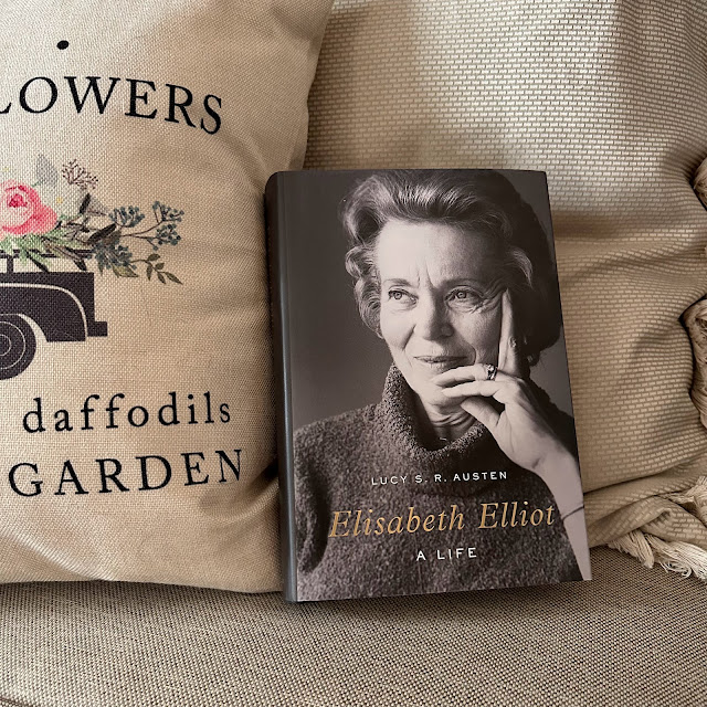 Hardcover book in front of cream throw pillows: the book is Elisabeth Elliot: A Life, by Lucy S. R. Austen. On the cover is a black and white photo of Elisabeth Elliot. Author’s name and “a life” are in white all caps. Elisabeth’s name is larger, italicized, and embossed in gold.