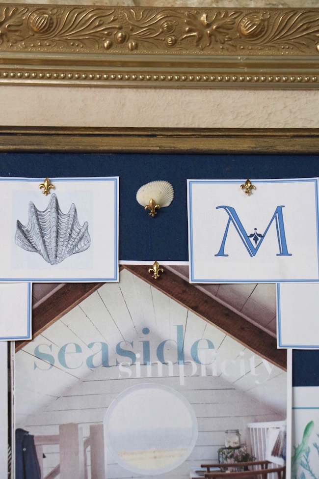 A fleur de lis pins a small white shell to a navy bulletin board to create a French Country coastal look for summer