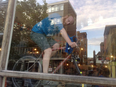 James Bowthorpe cycling in the window of Look Mum No Hands in the Evening