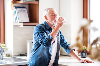 Elderly man drinking a glass of water in the kitchen