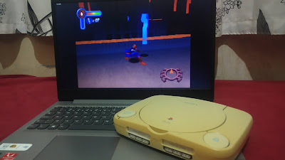 Foto de um PS1 em cima de um notebook com o jogo Spider-Man 2 no computador