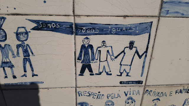 azulejos brncos com pinturas em azul de várias pessoas e a frase: Somos Todos Iguais