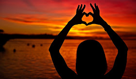 Girl holding up fingers to make a heart shape into sunset 