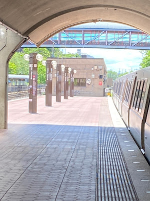 Photo of the train platform. There is a Metro train on the right side and several pillars identifying the station as Silver Spring. There is a covered platform on the other side of a fence visible on the left.