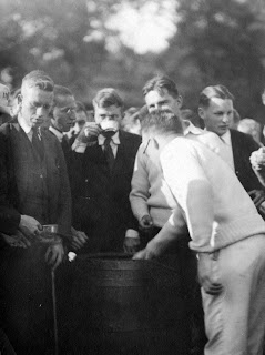 A photograph of a crowd of men filling cups from a keg.