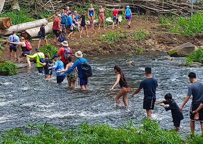 Line of hikers crossing a river using a rope bridge