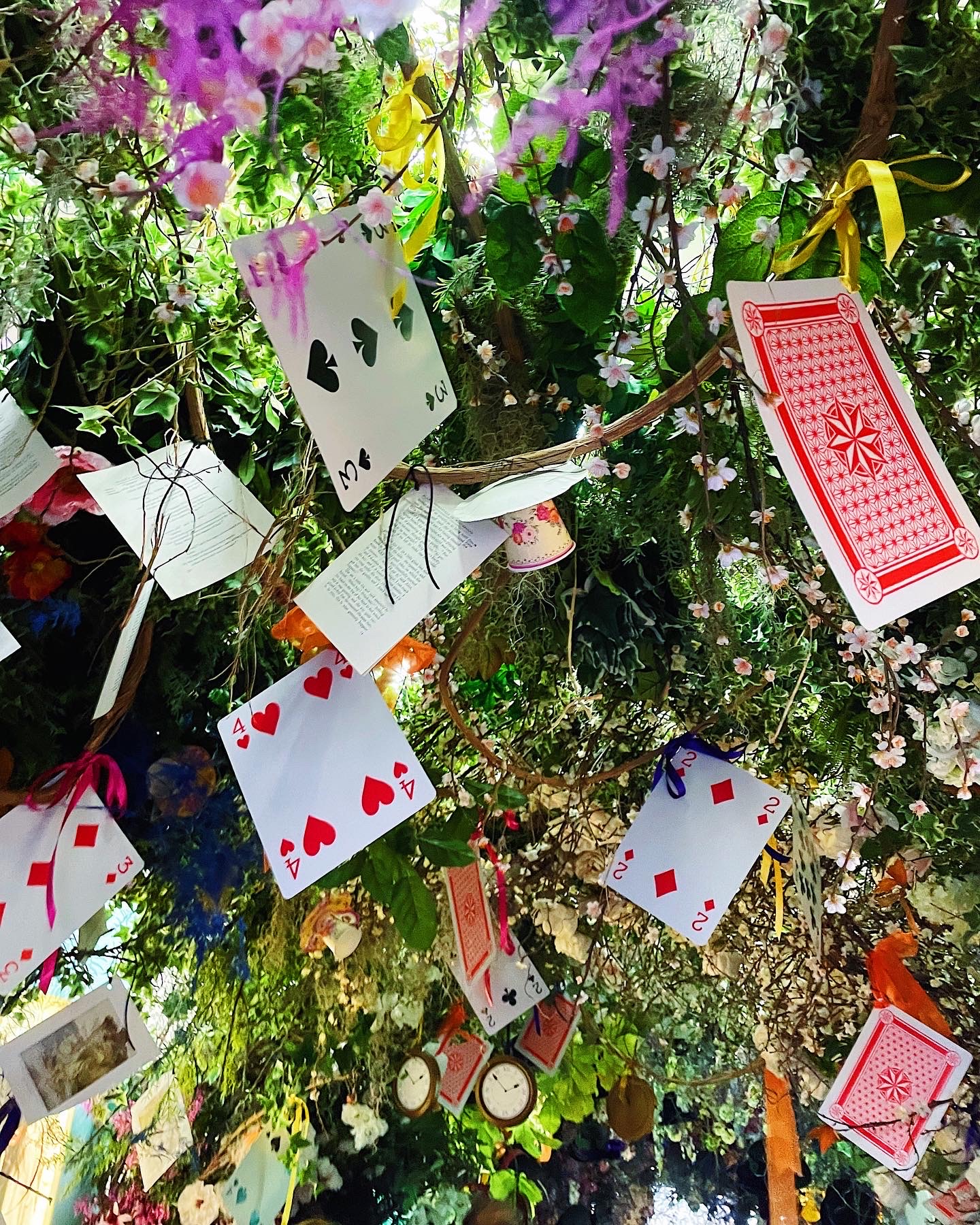Giant playing cards and teacups hanging from an overhead floral canopy.