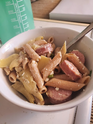 A white bowl full of a pasta salad with whole wheat penne and chicken sausage visible