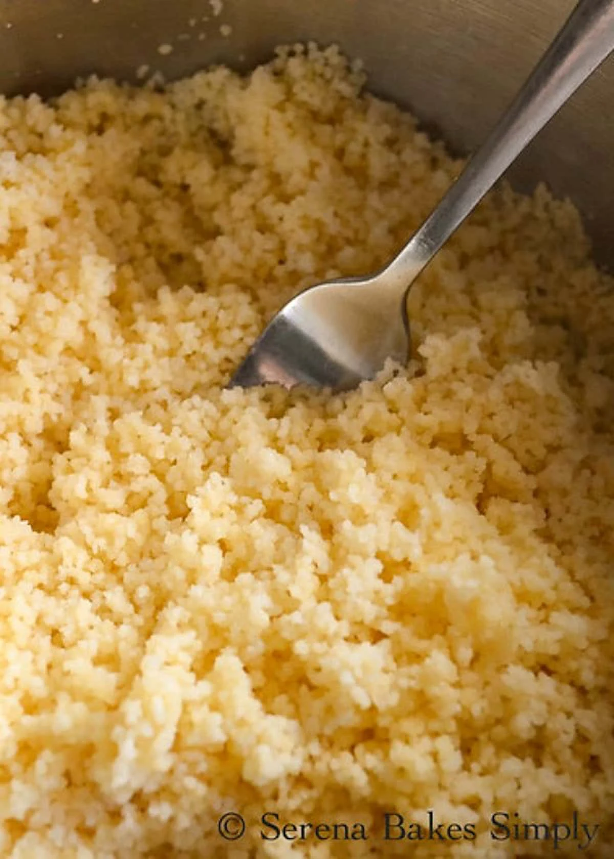 A down shot of Couscous being fluffed in a stainless steel pan with a fork.