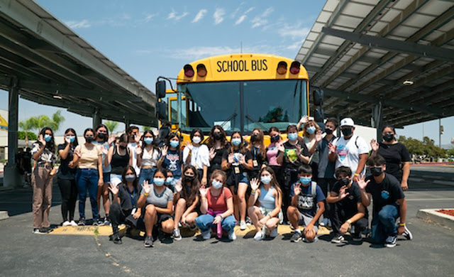 Many students stand in front of an electric bus