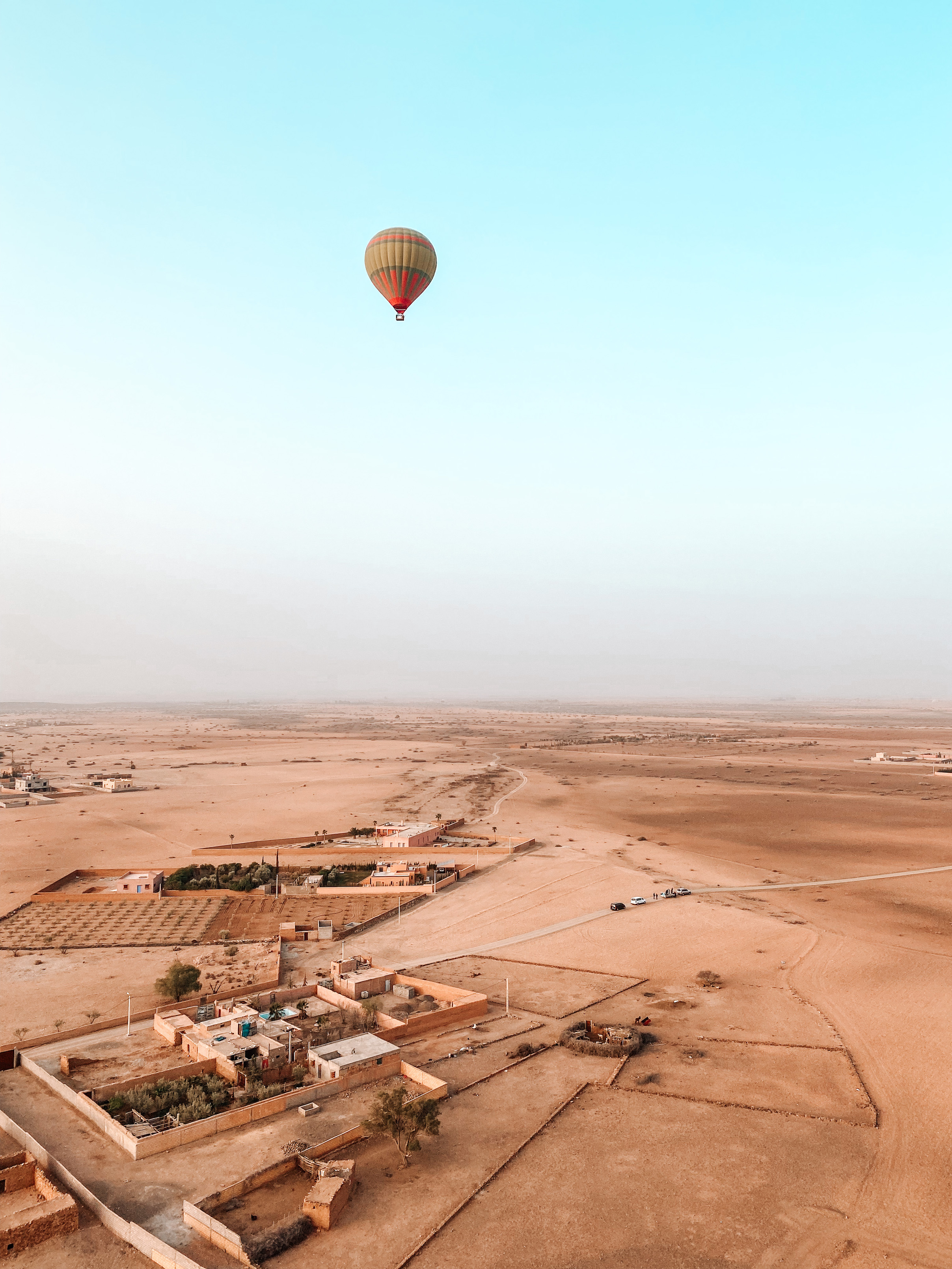 une montgolfière verte et orange qui survole la palmeraie de marrakech