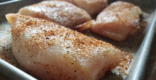 Fresh red snapper pieces on a baking sheet covered with seasonings.