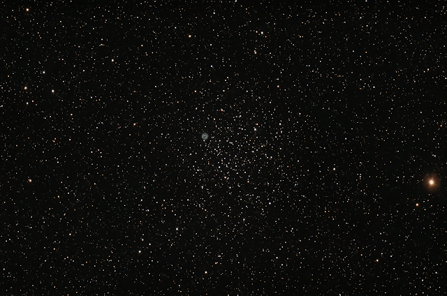 A telescopic image of a cluster of stars on the left edge of the cluster is a small circle of colored gas.