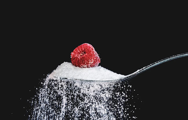 A raspberry carefully placed on a spoon full of sugar.