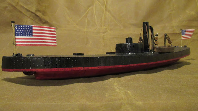 A model boat, black above and red below, with a curved deck and a cylindrical turret.